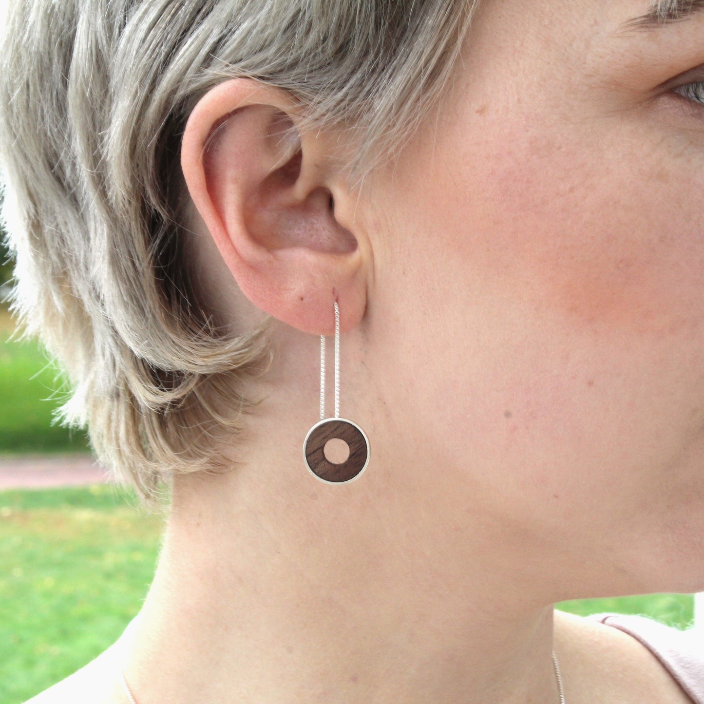 Close-up of a person wearing a dangling earring with a park in the background