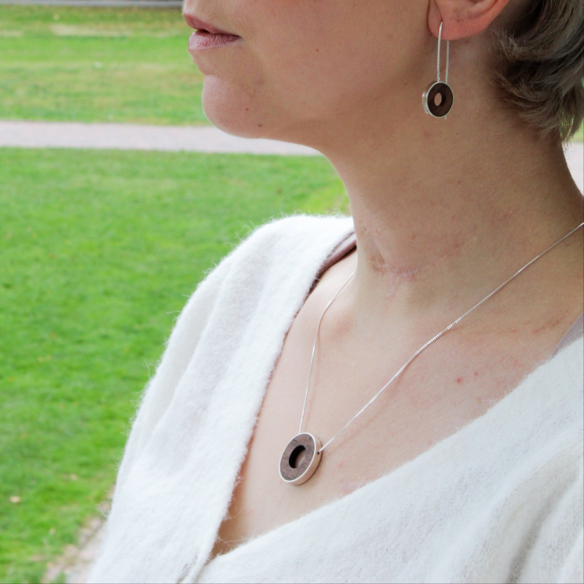 Circle pendant and earring set on woman with short hair with a park in the background 