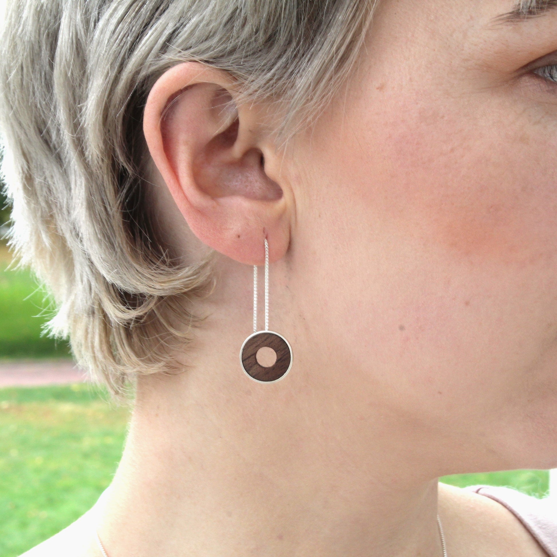 Close-up of a person wearing a dangling earring with a park in the background