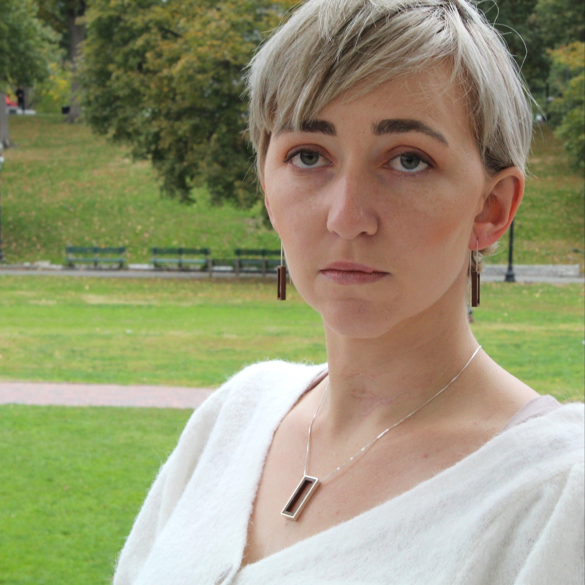 Person with short hair standing in a park wearing wood and silver jewelry 