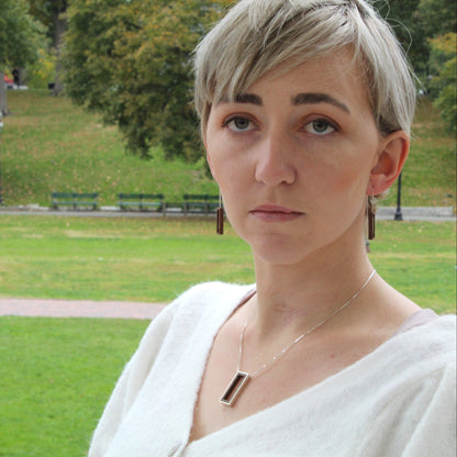 Person with short hair standing in a park wearing wood and silver jewelry 