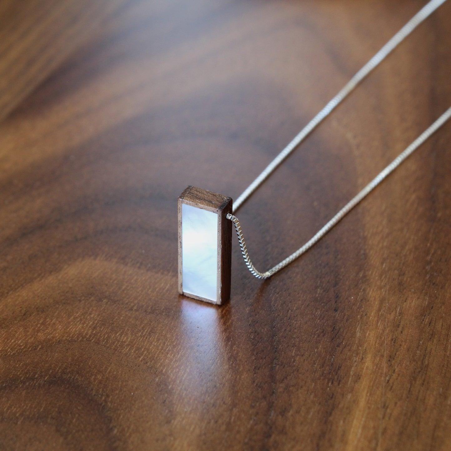 Rectangular pendant on a chain on a wooden surface