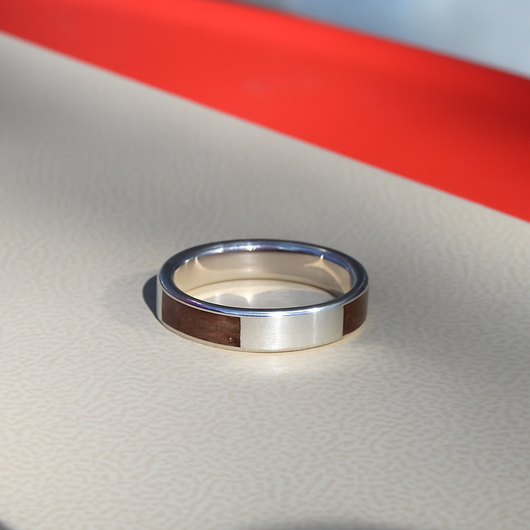 Silver ring on a reflective surface with a red stripe in the background
