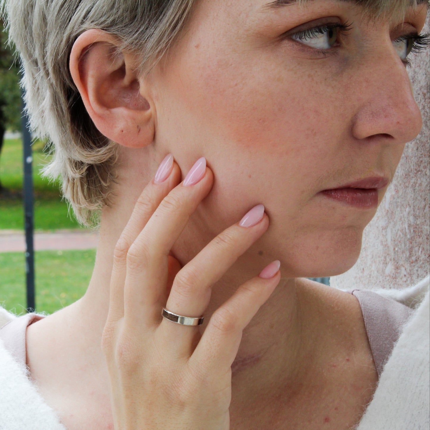 Woman with short hair and a ring on her finger, outdoors in a park.