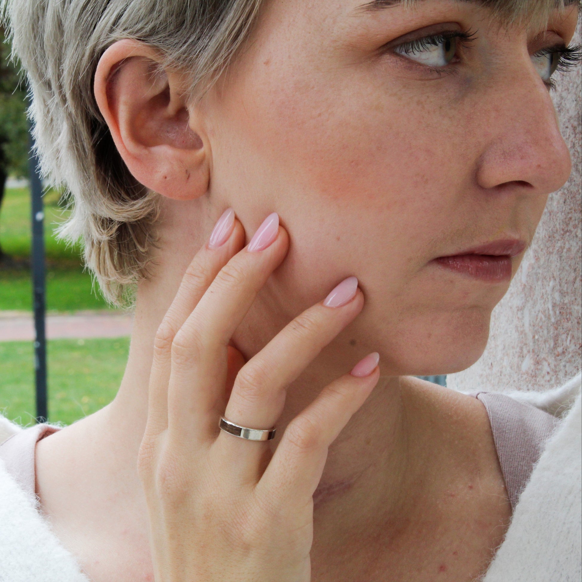 Woman with short hair and a ring on her finger, outdoors in a park.