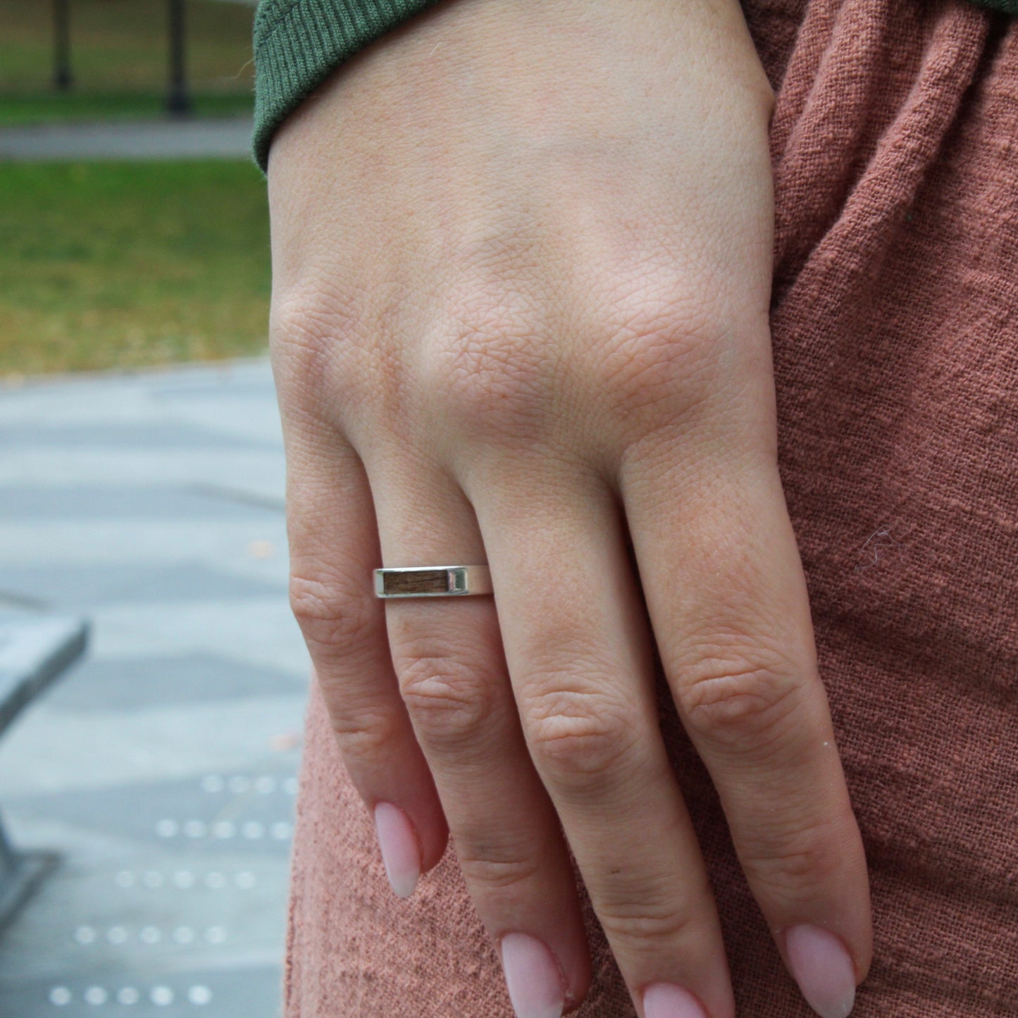 Close-up of a hand wearing a ring with a blurred outdoor background