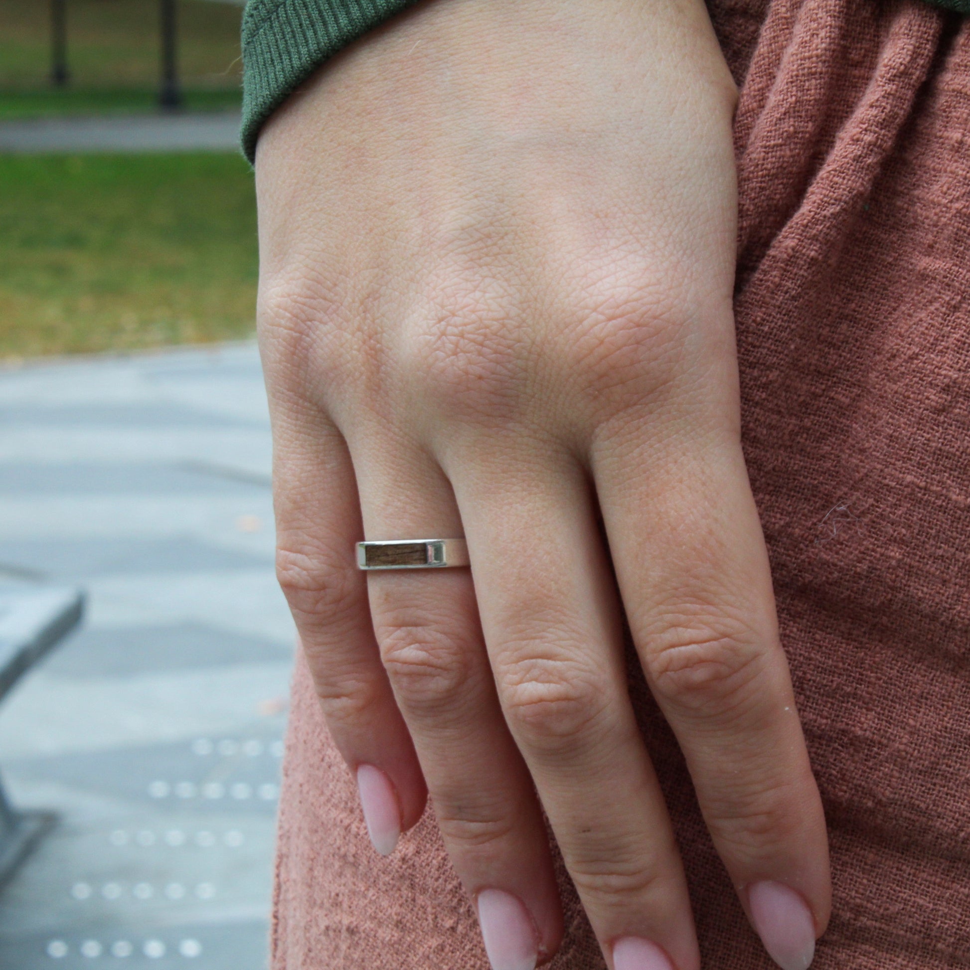 Close-up of a hand wearing a ring with a blurred outdoor background