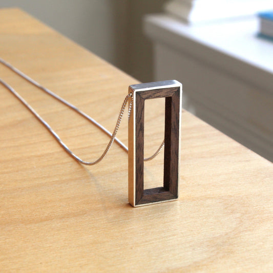 Silver necklace with a rectangular pendant on a wooden surface