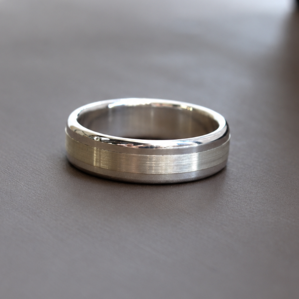 A silver-toned metal band ring with a brushed center and polished beveled edges, resting on a dark gray surface.